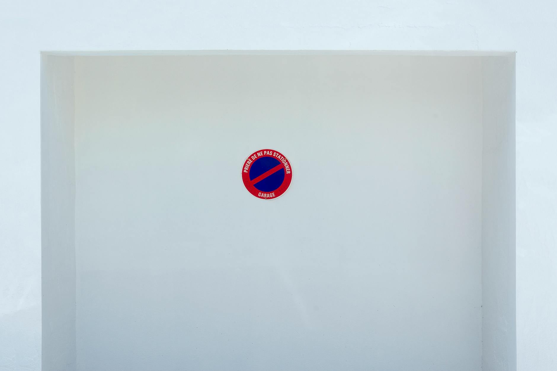 Simple no parking sign on a white wall background, emphasizing minimalism and space.