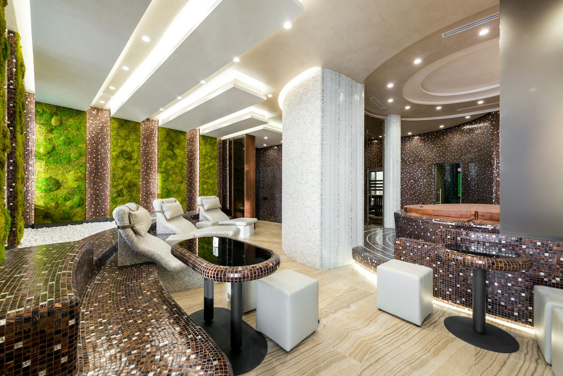 Comfortable heated tiled chaise lounges and bathtubs in modern luxurious spa center decorated with creative illumination and fresh green plants on walls