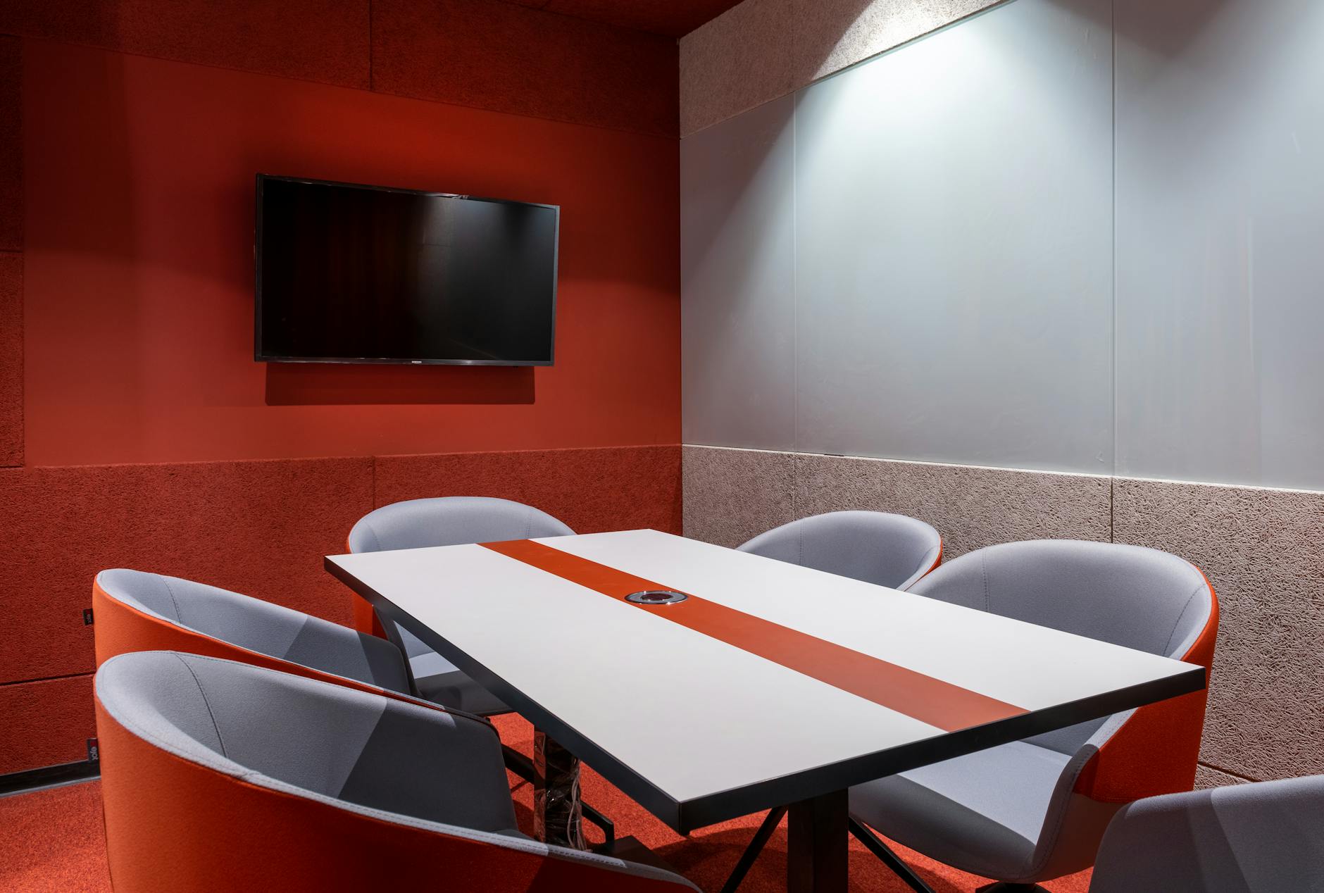 Orange comfortable chairs placed around white table against red wall with TV in stylish office of contemporary financial business center