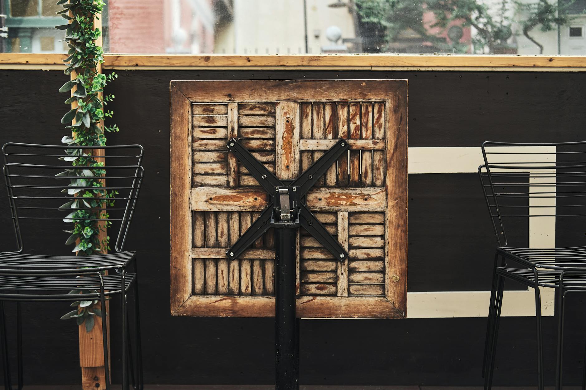 Closed café terrace with a folded wooden table and metal chairs, ideal for urban outdoor settings.