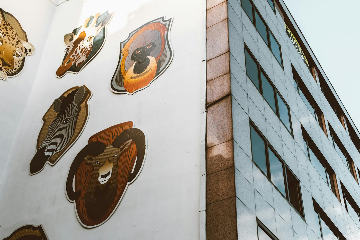 Creative animal mural displayed on the side of a city skyscraper, featuring diverse wildlife.
