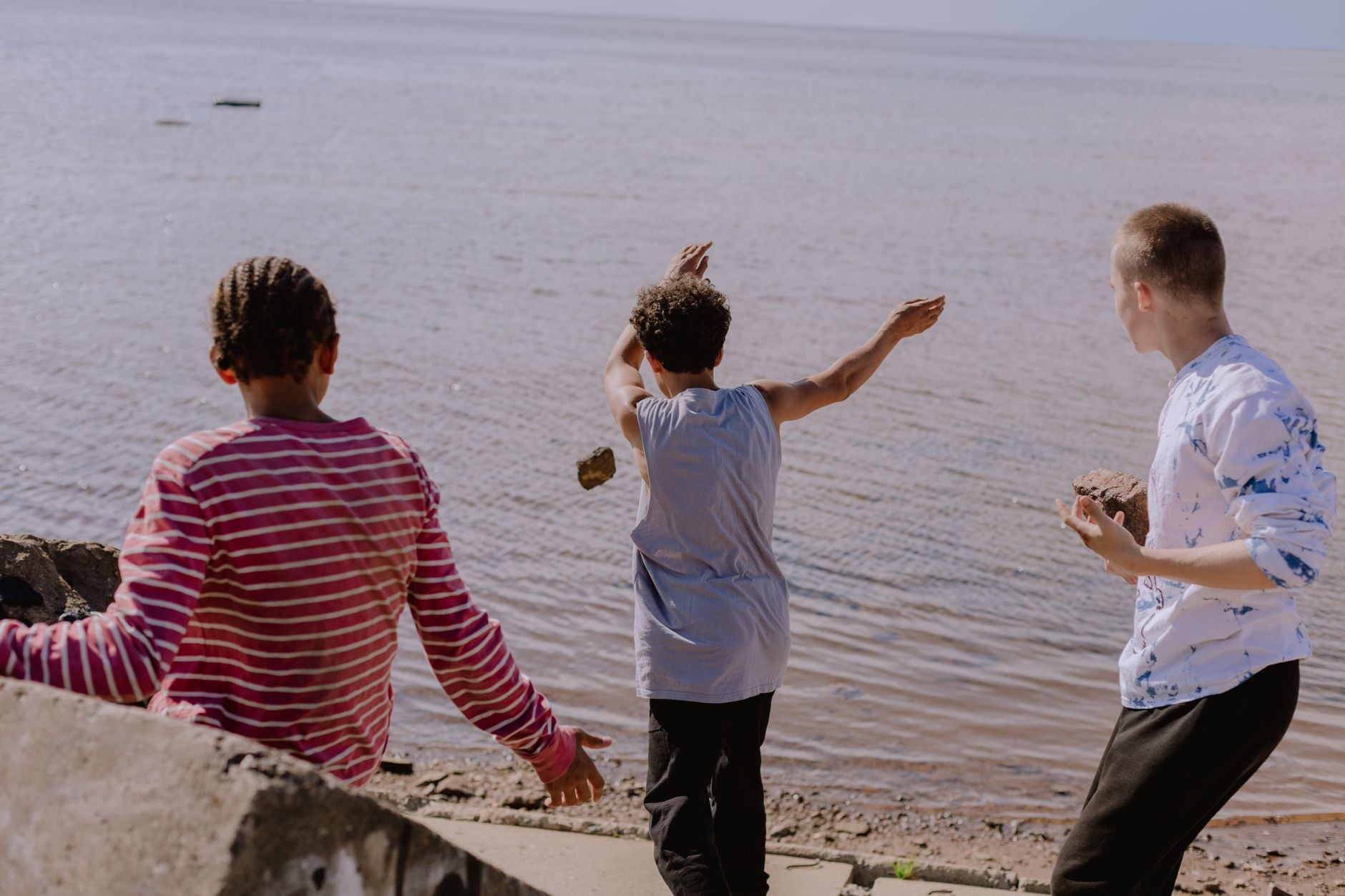Three boys enjoying a carefree day by the river, joyfully skipping rocks together.