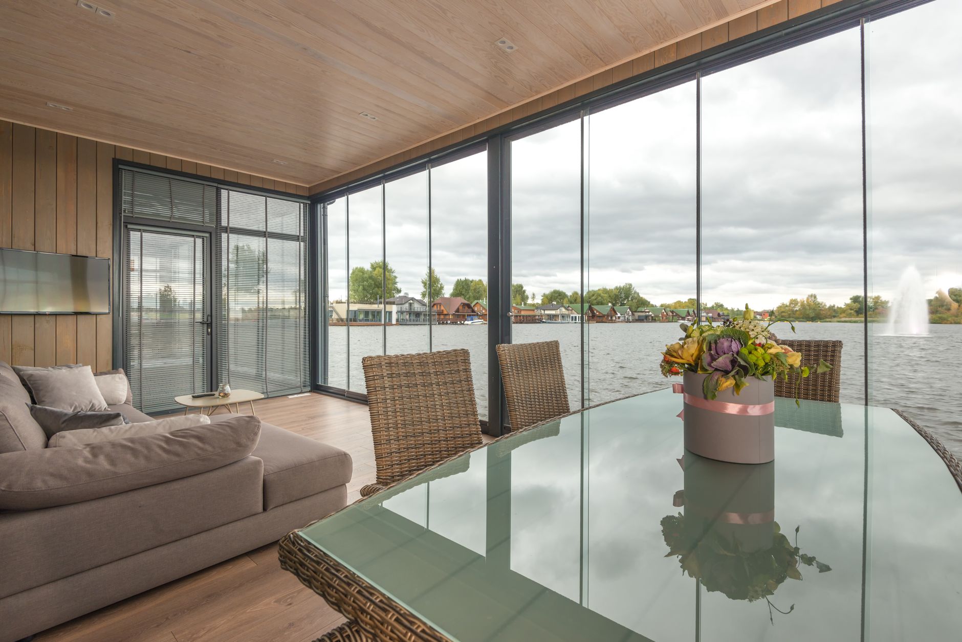 Elegant flowers bouquet placed on table with glass top in contemporary house with soft sofa and glass walls located on lake under overcast sky