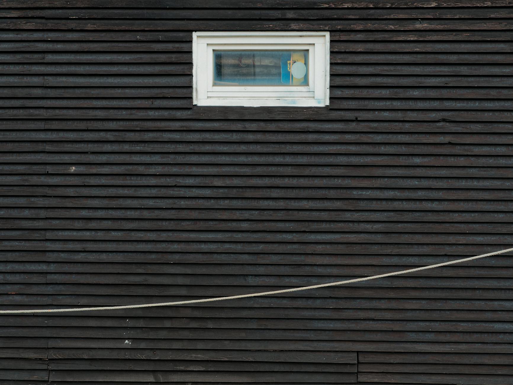 Dark wooden wall featuring a single rectangular window in a minimalist architectural style.