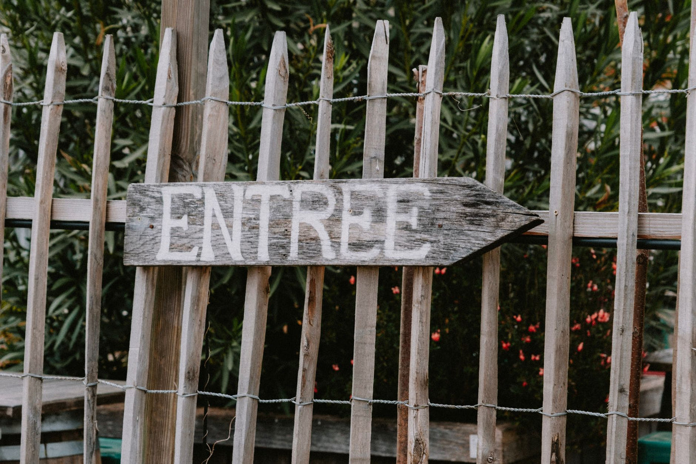 Weathered wooden sign with the word 'ENTREE' pointing direction in a garden setting.
