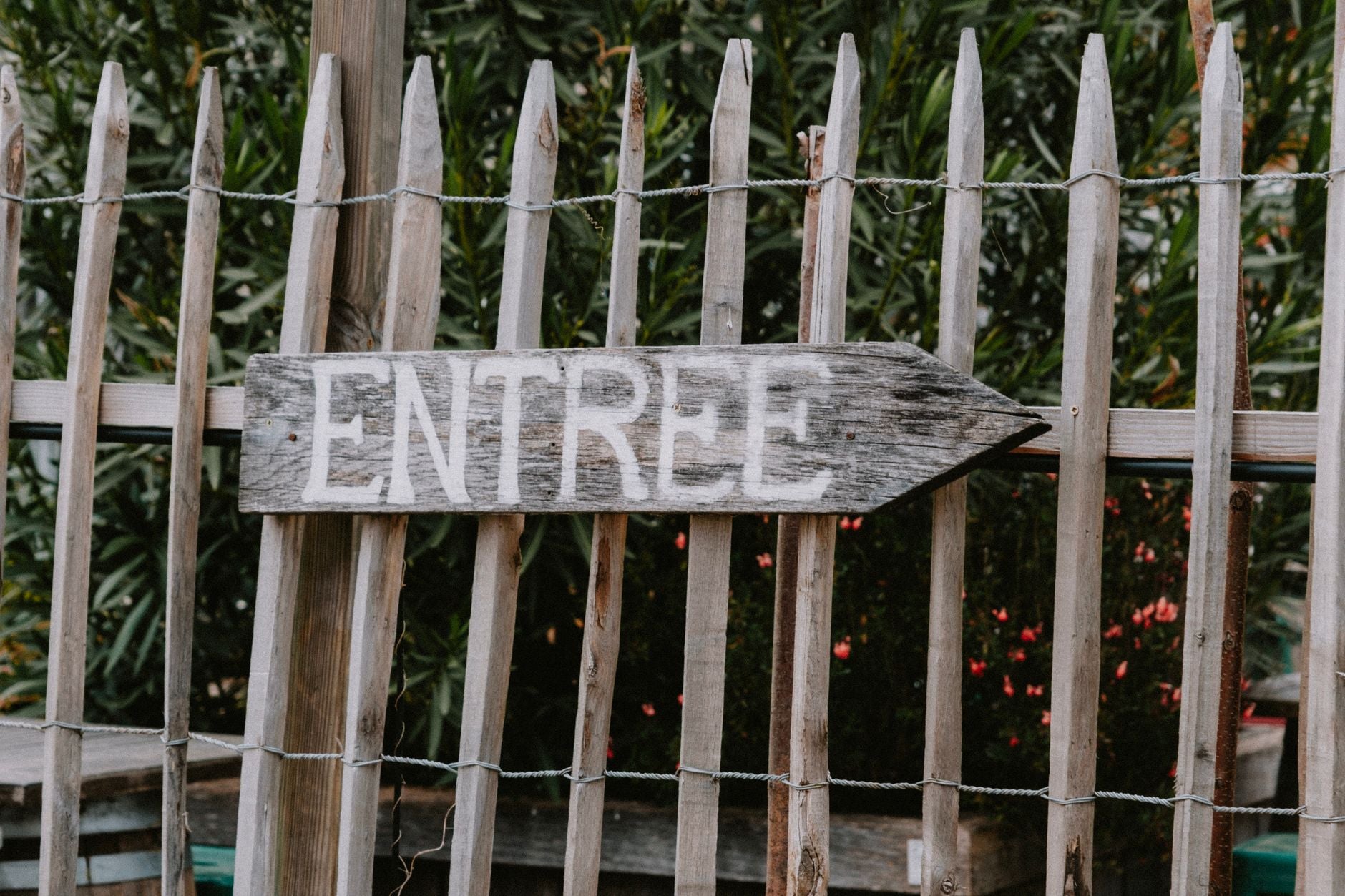 Weathered wooden sign with the word 'ENTREE' pointing direction in a garden setting.