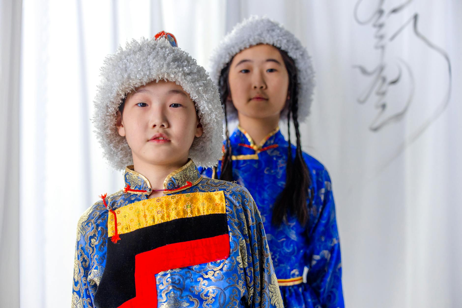 Two children in traditional Mongolian clothing with fur hats, showcasing cultural heritage.