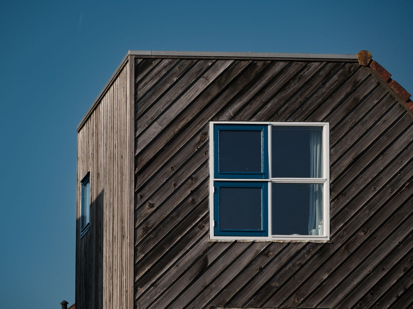 Minimalist wooden house exterior with blue window against clear sky.