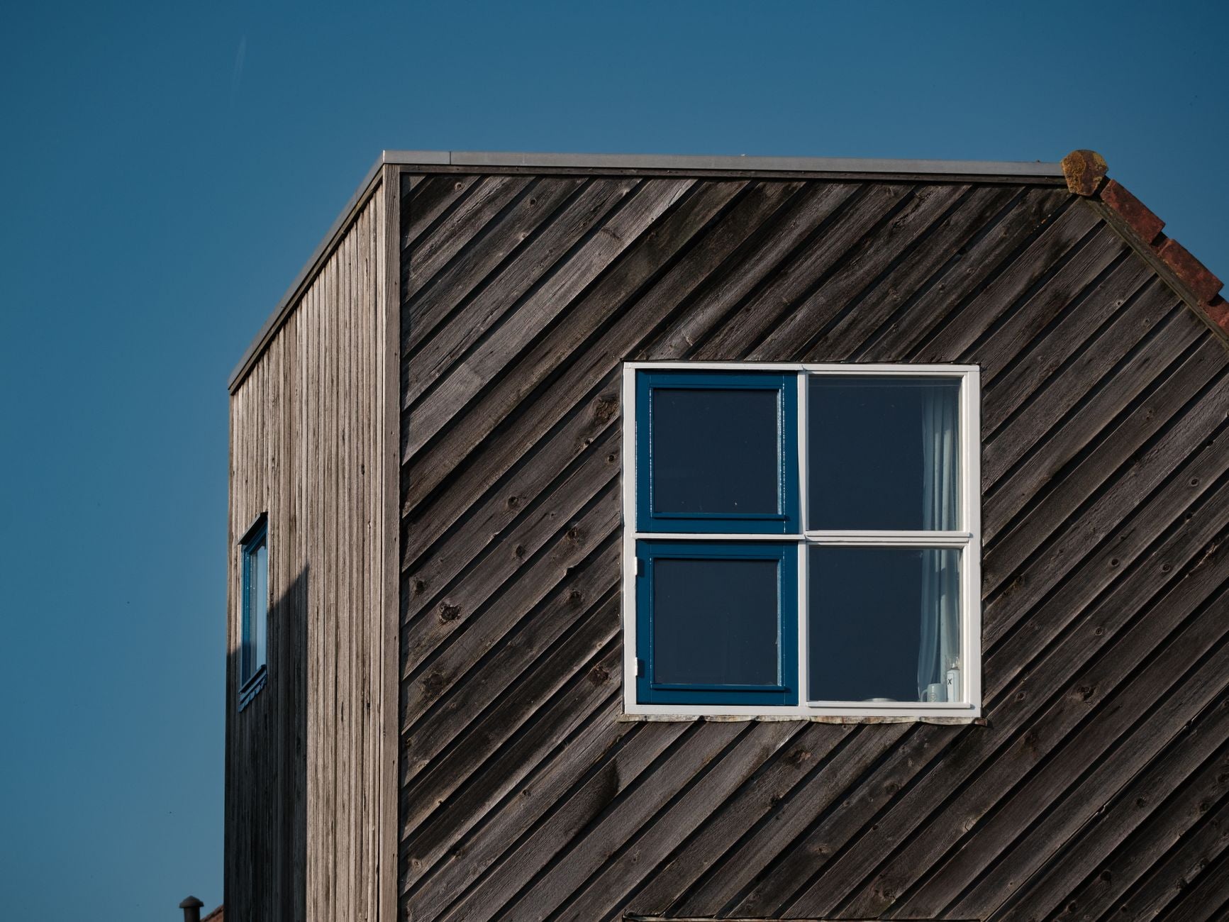 Minimalist wooden house exterior with blue window against clear sky.