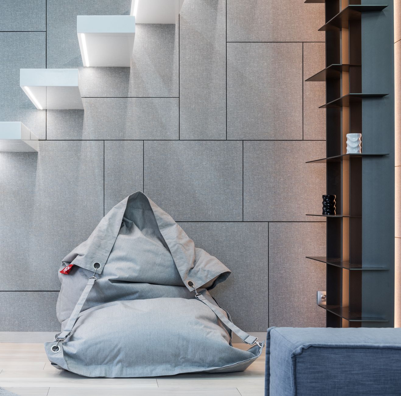 Interior of modern light living room with bean bag chair placed on floor near steps and shelves with various decorations