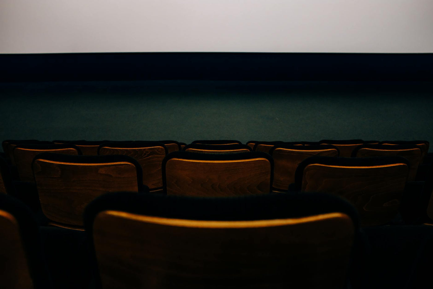 An empty auditorium with wooden seats facing a blank theater screen.