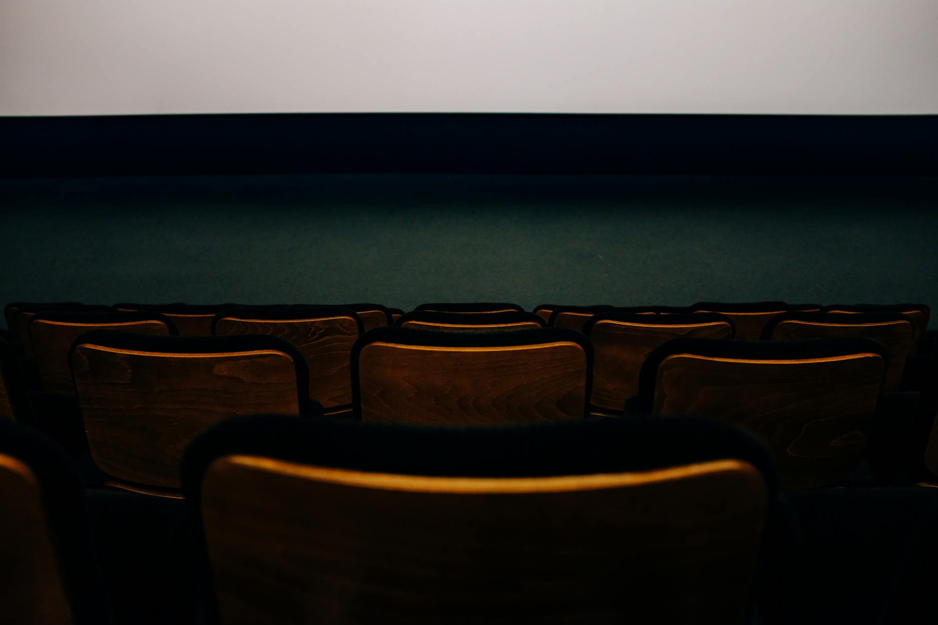 An empty auditorium with wooden seats facing a blank theater screen.