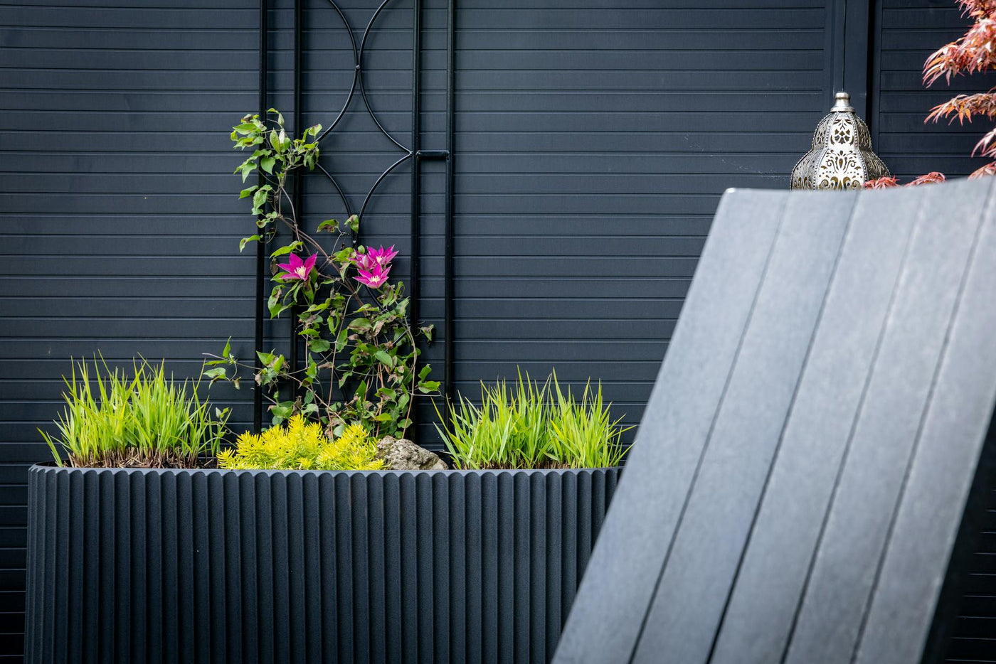 Stylish planter with vibrant pink flowers and lush greenery against a dark textured background.