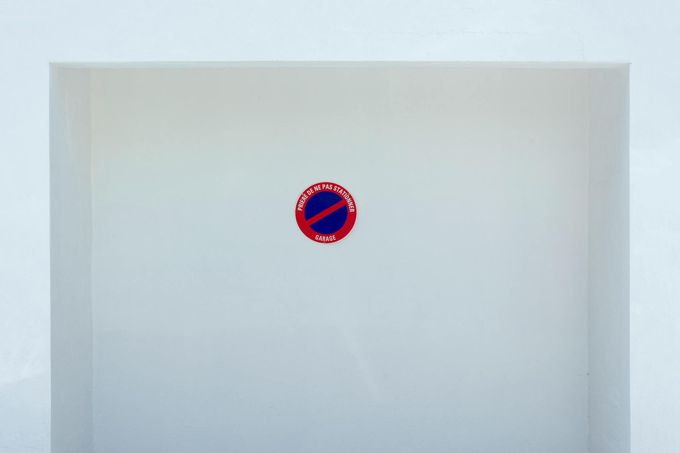 Simple no parking sign on a white wall background, emphasizing minimalism and space.