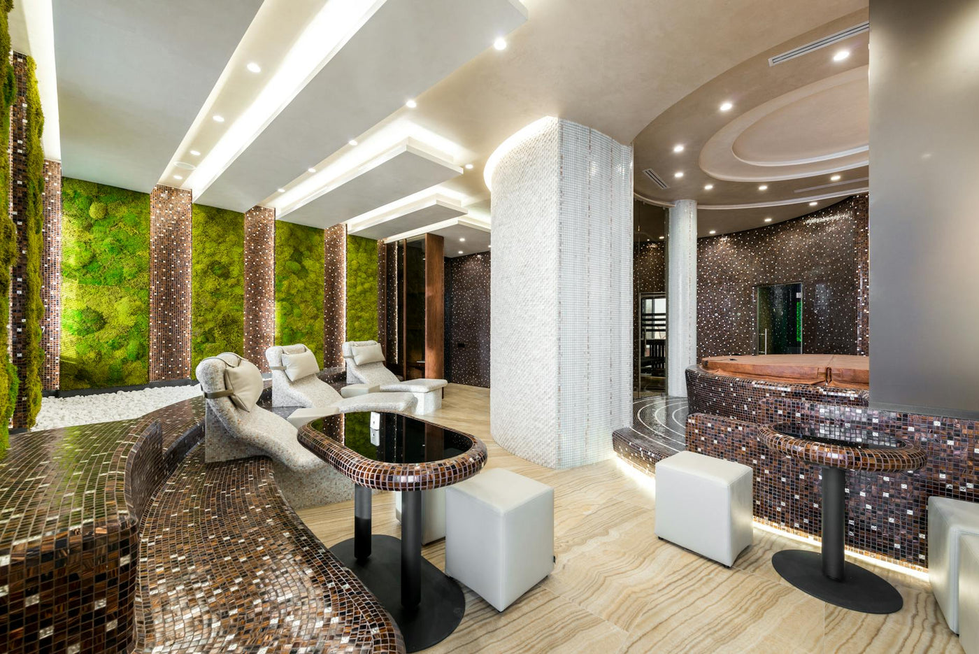 Comfortable heated tiled chaise lounges and bathtubs in modern luxurious spa center decorated with creative illumination and fresh green plants on walls