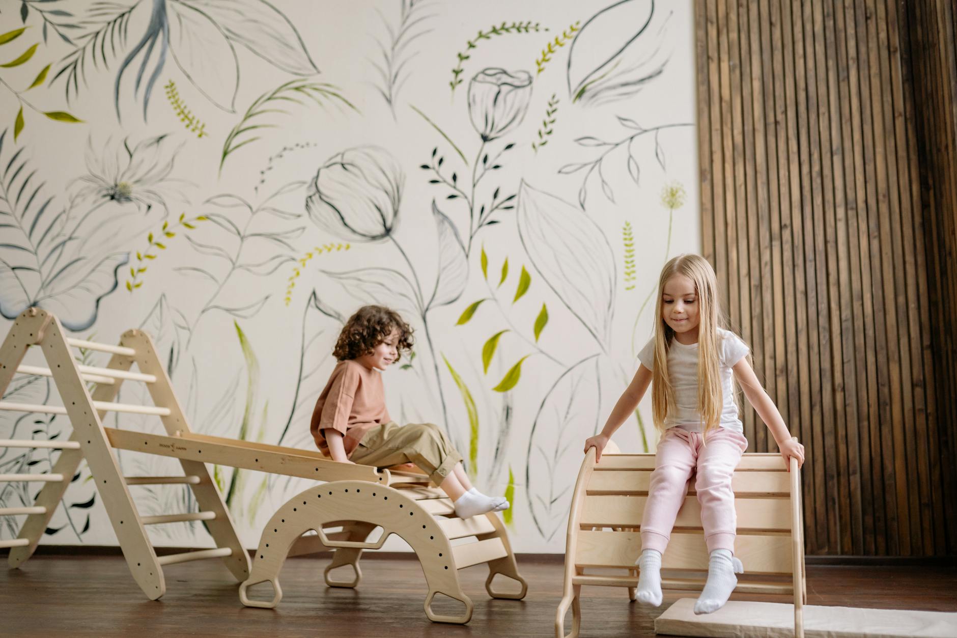 Two children enjoying a wooden slide in a stylish indoor playroom setting.
