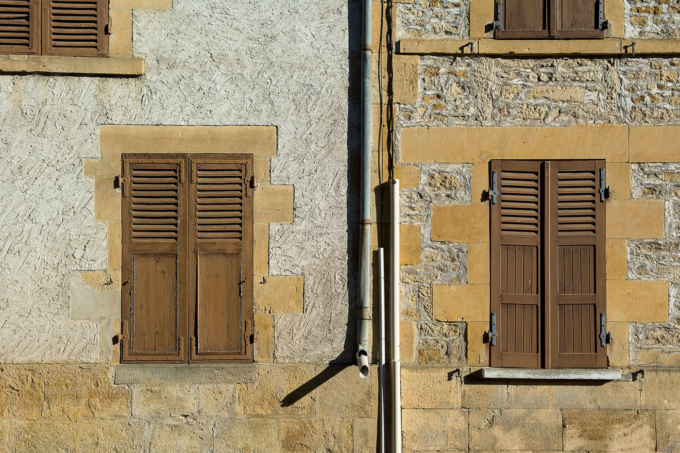 Close-up of a vintage stone facade with wooden shutters, showing rustic charm.