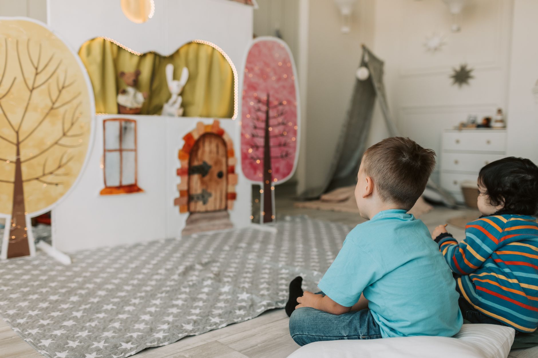 Two children watching a charming indoor puppet show with colorful backdrop.