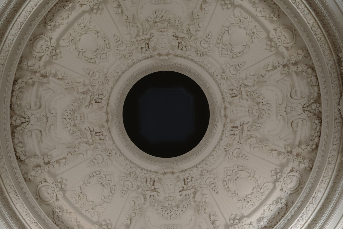 Intricate neoclassical ceiling with ornate bas reliefs and central circular feature in classical architecture.