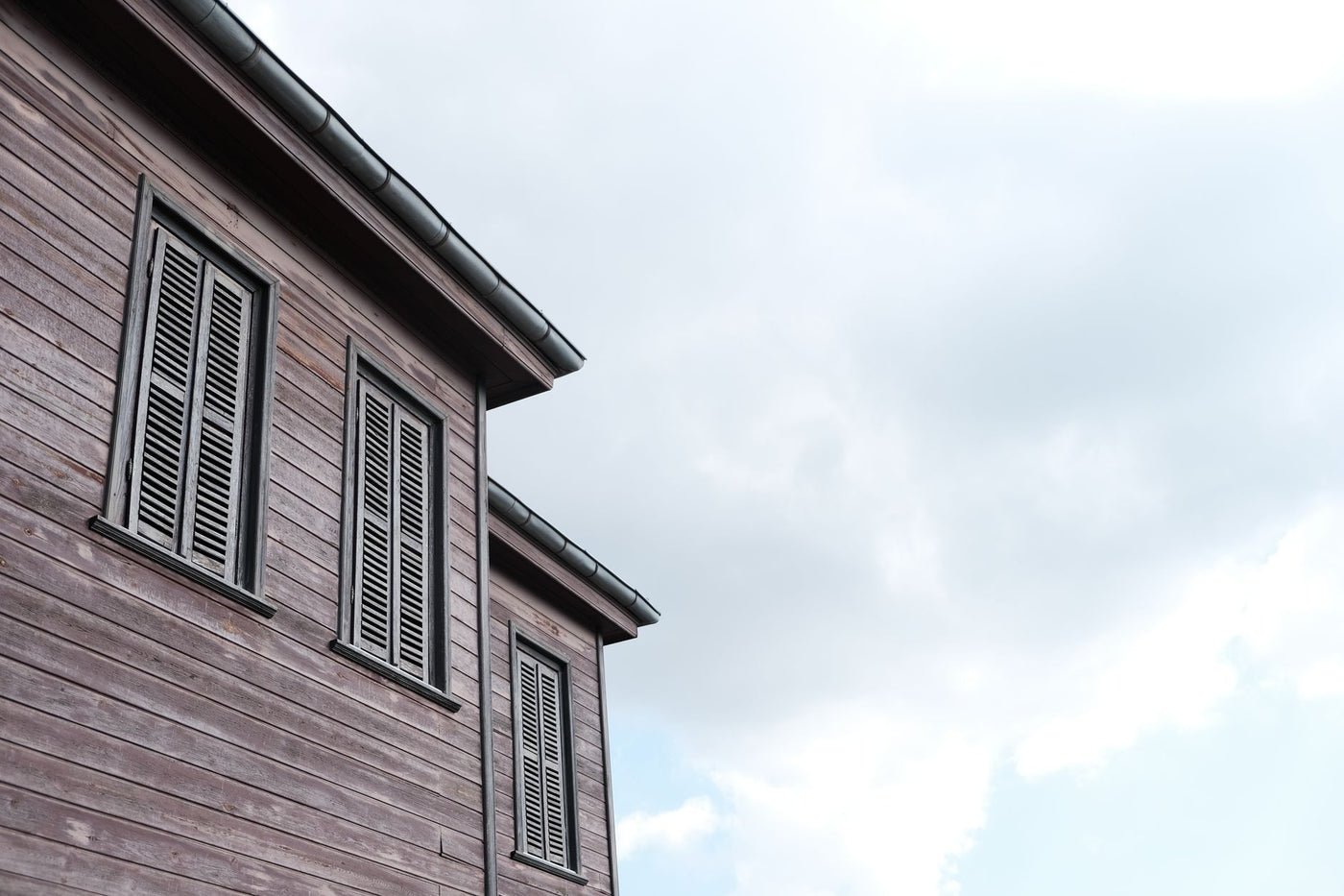Low angle view of a traditional wooden house with shutters against a partly cloudy sky.