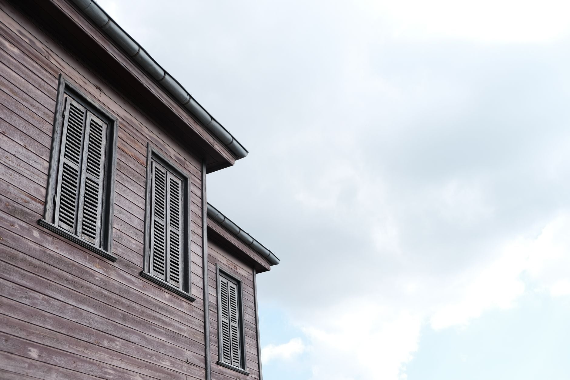 Low angle view of a traditional wooden house with shutters against a partly cloudy sky.