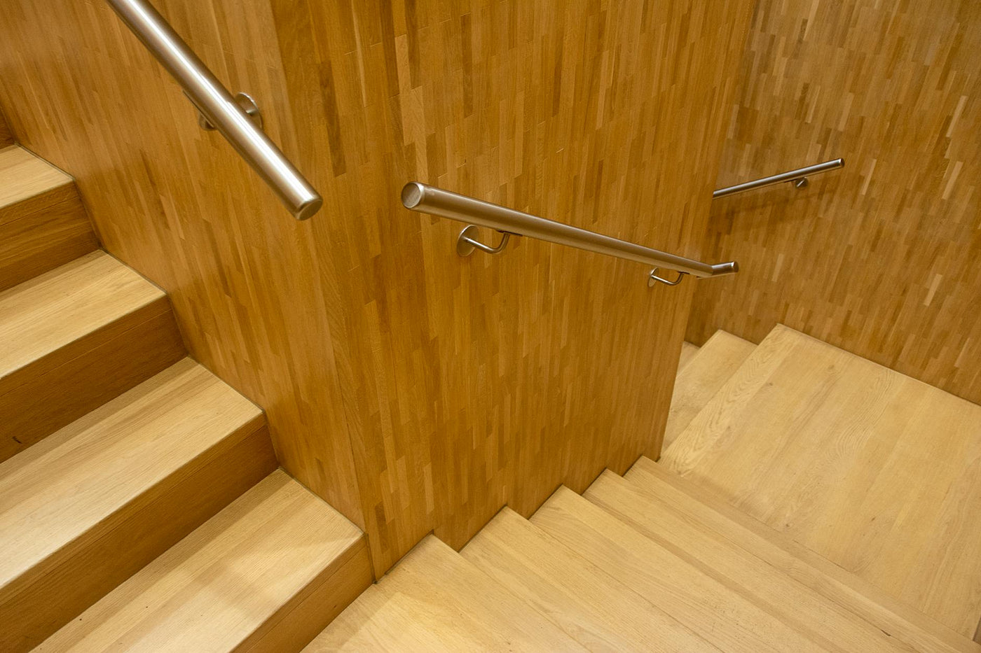 Contemporary wooden staircase with sleek metal handrails in an indoor setting.